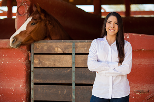 woman standing in barn with horse behind her